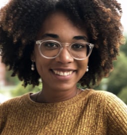 Young black woman wearing yellow sweater with clear rim eyeglasses smiling