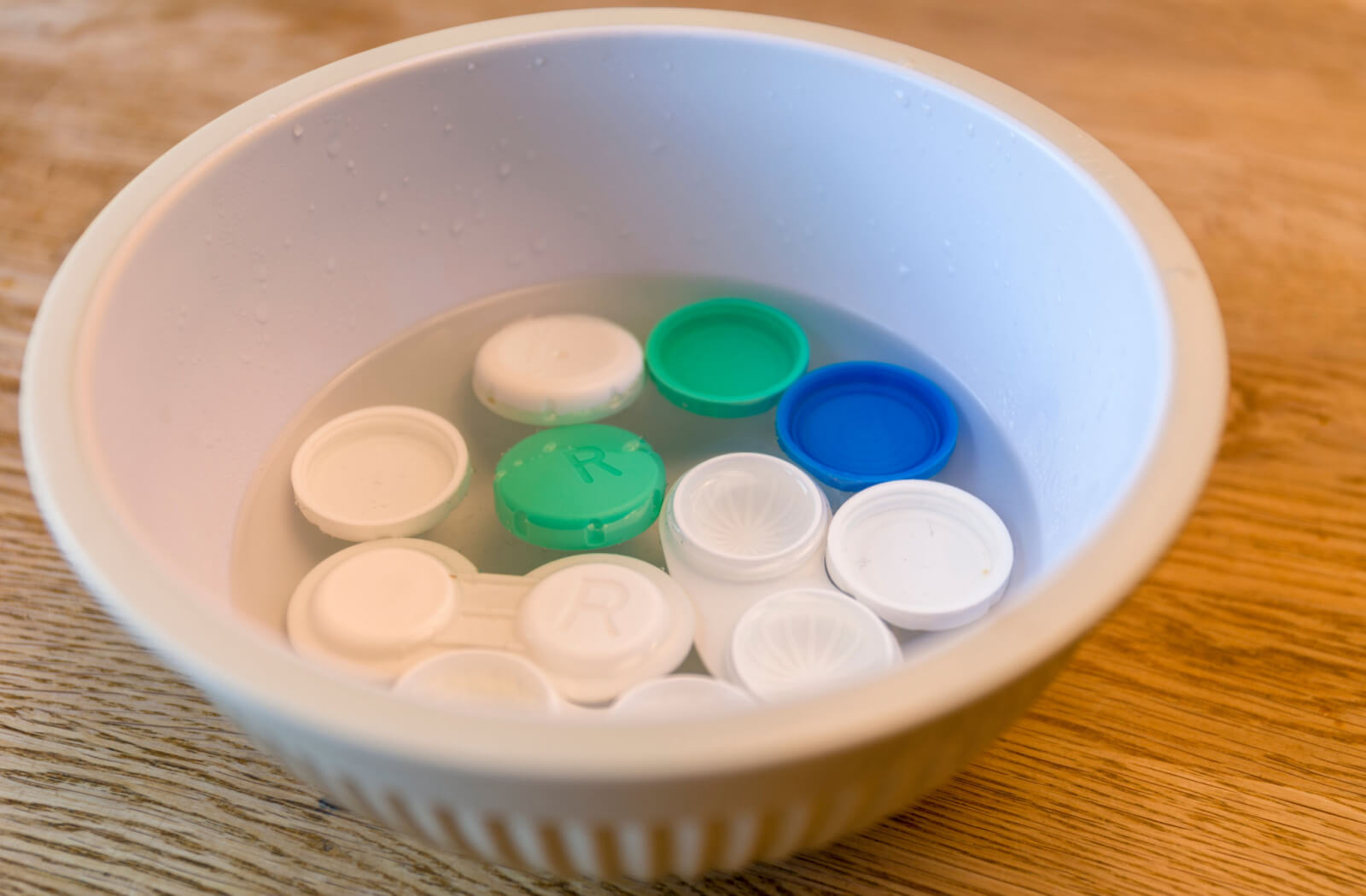 Several contact lens cases are being cleaned and sterilized in a bowl with just boiled steaming hot water before storing contact lenses in it.
