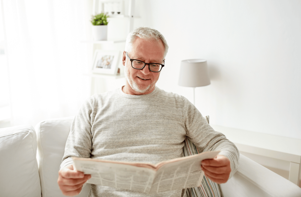 A middle-aged man uses reading glasses to read a newspaper