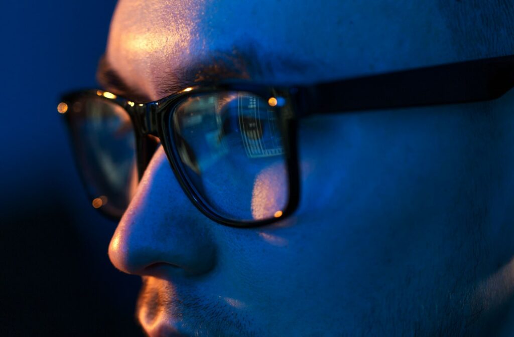 A young man wearing glasses with blue light protection on them to prevent eye strain from screens