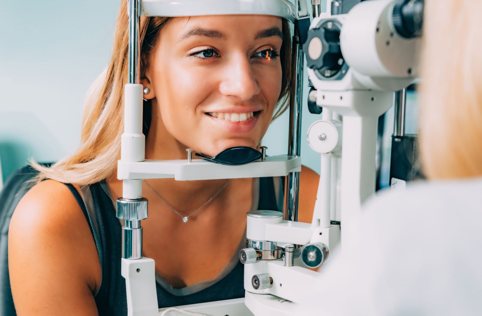 A young woman is undergoing a retinal exam with the use of a slit lamp.