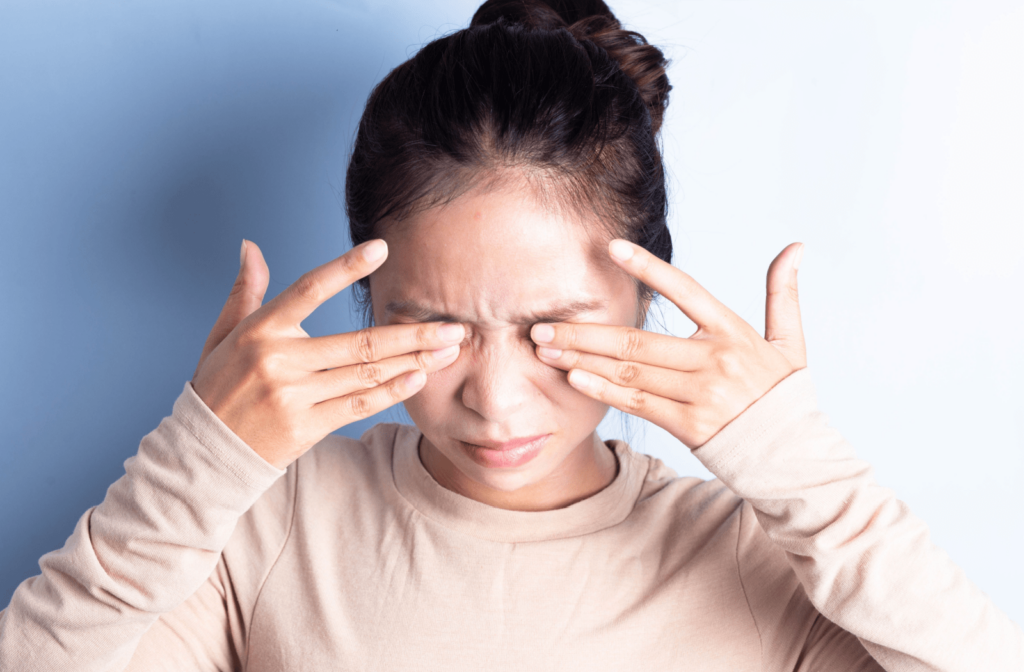 A woman against a white background rubbing her eyes with both hands.