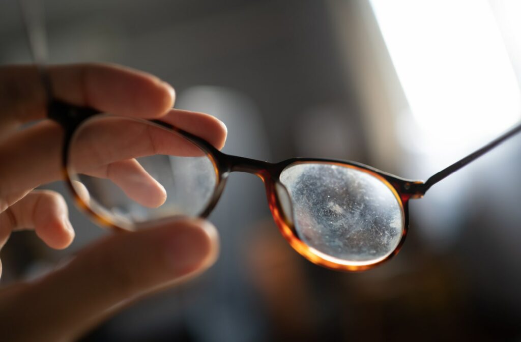 A close-up of a dirty pair of eyeglasses being held by a woman.