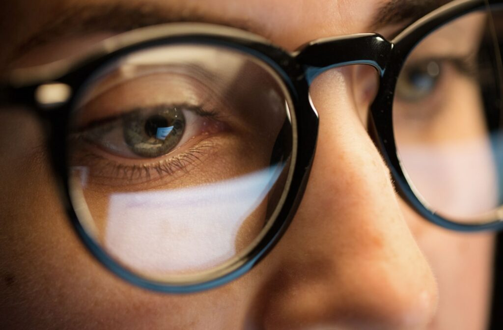 An intense close-up of a woman wearing glasses. Her glasses reflecting her computer screen.