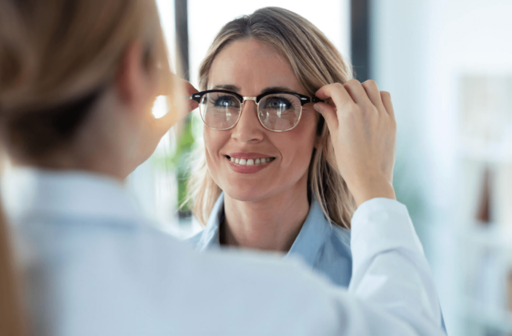 A female optician is helping a woman try on new eyeglasses.