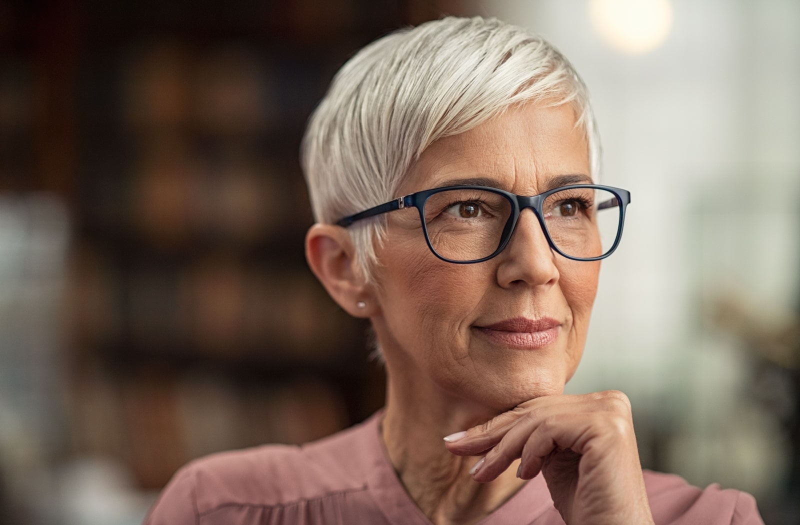 An older adult woman with gray hair, thinking and wearing eyeglasses.