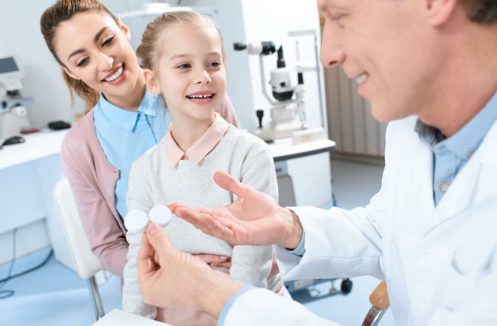 An eye doctor holding a contact lens case explaining how to use contact lenses to a child and her mother.