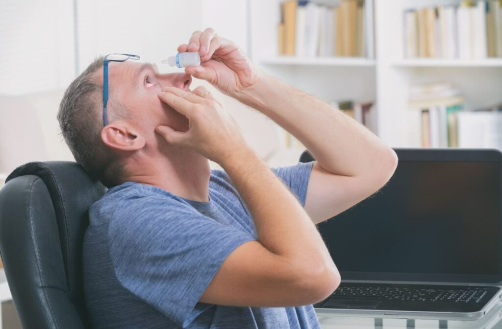 A person applying eye drops to relieve dry eye symptoms while sitting at a desk.