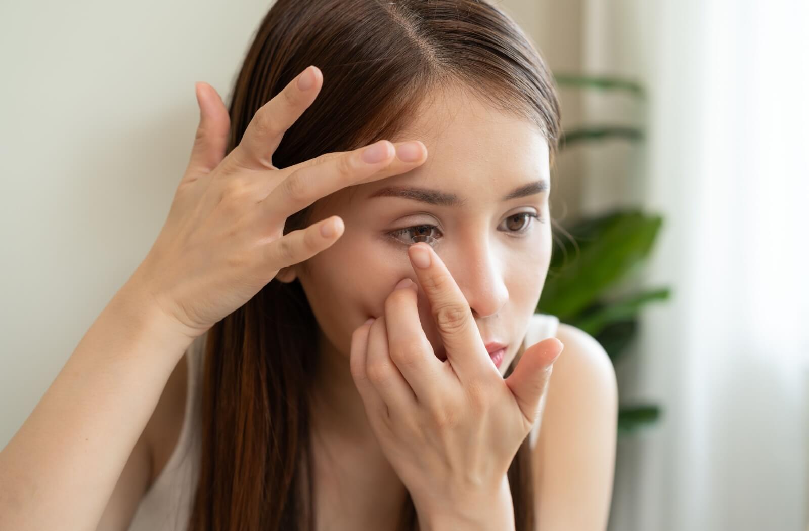 A close-up of a woman carefully inserting a contact lens into her eye.