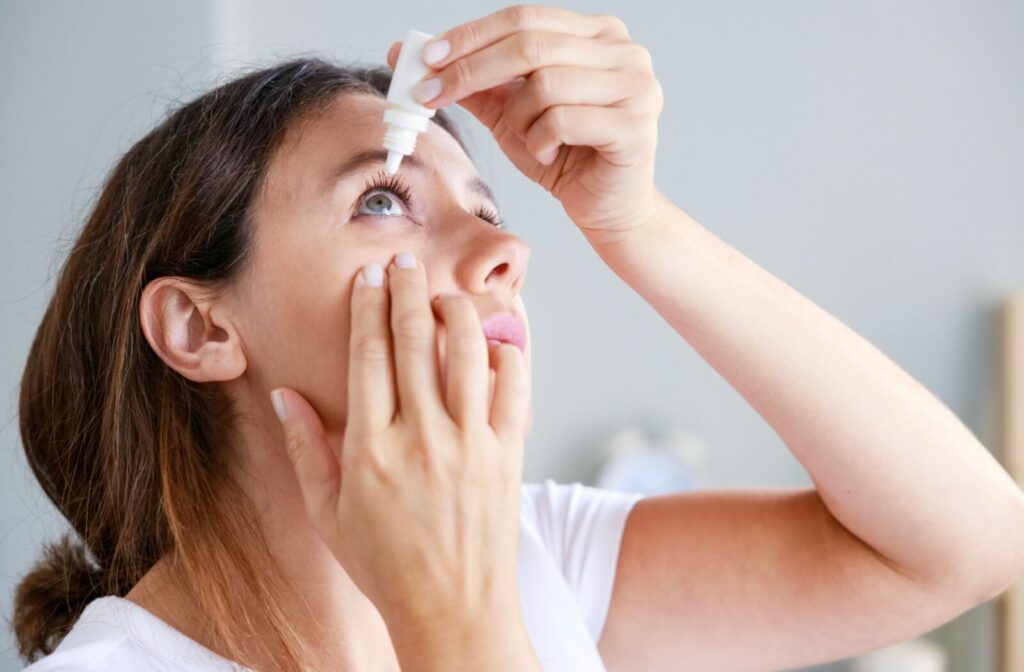 A person gently pulls down their eyelid and prepares to apply eye drops.
