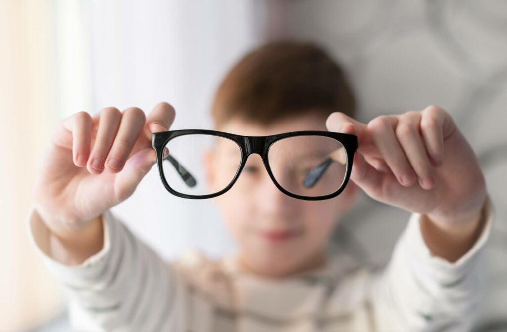 A child holding up a pair of myopia eyeglasses.