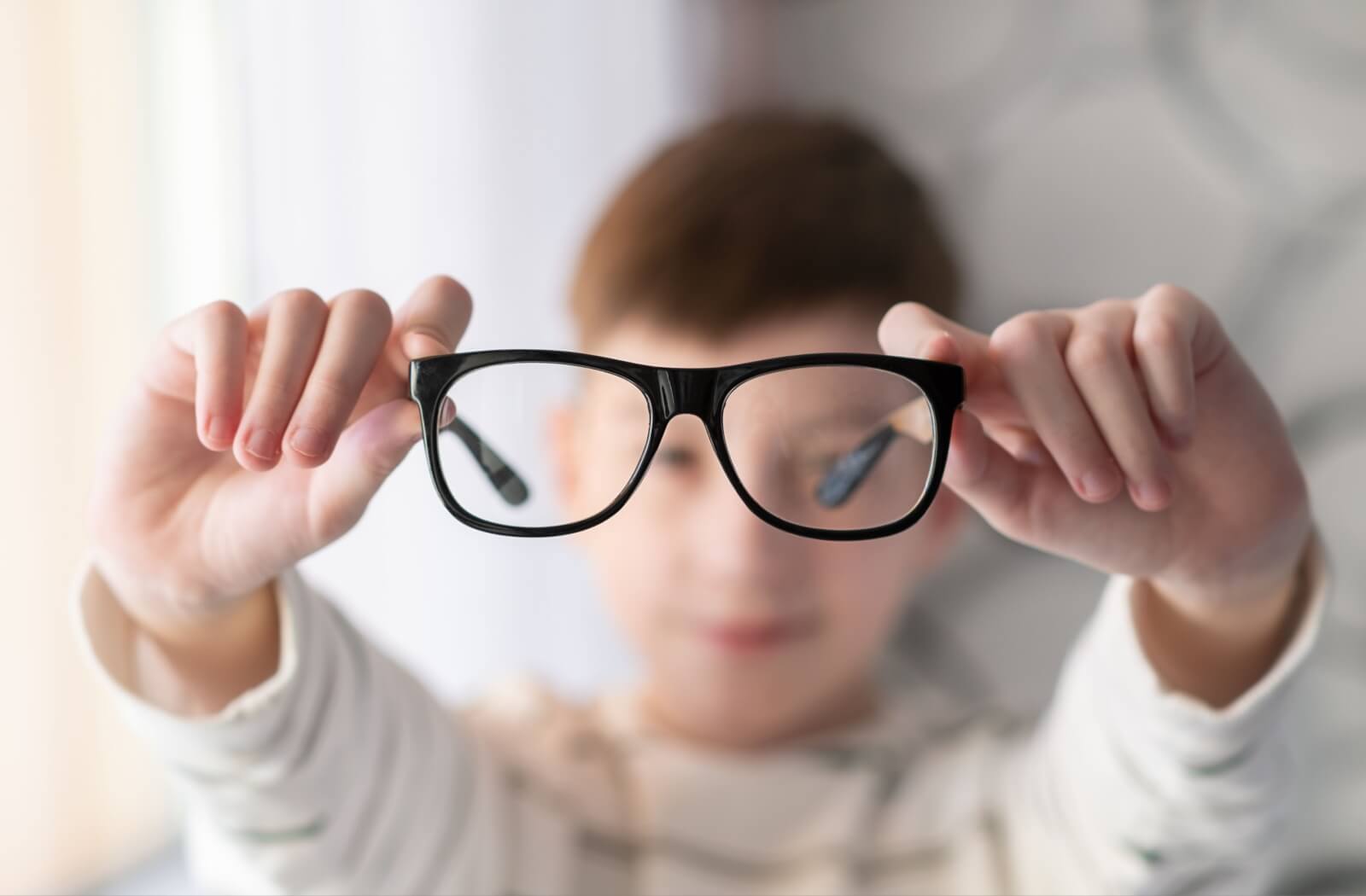 A child holding up a pair of myopia eyeglasses.