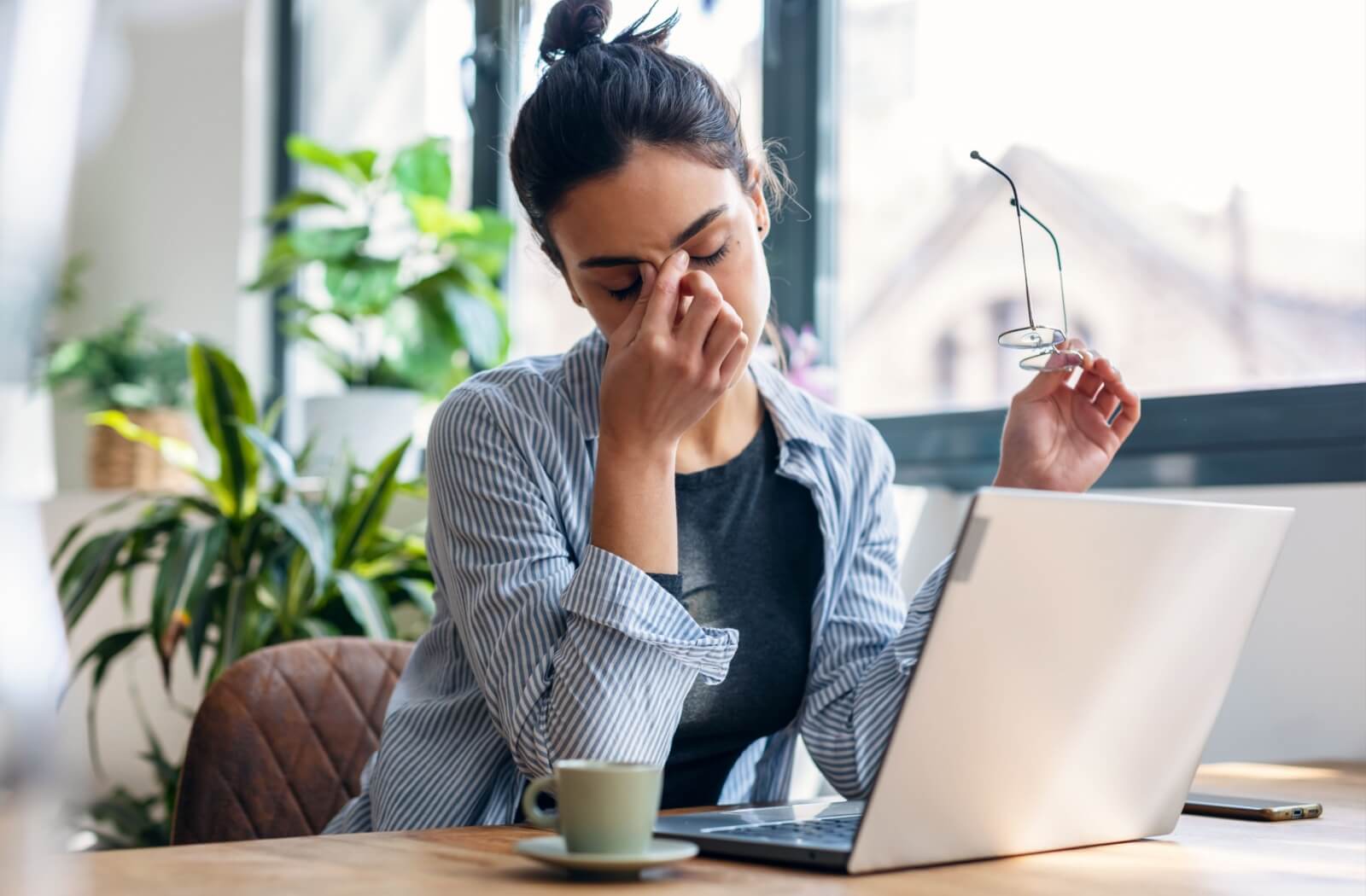 Person using a laptop with eyeglasses in hand and eyes closed.