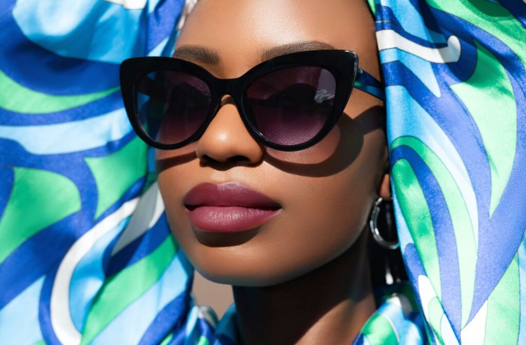A person wearing a vibrant blue and green patterned headscarf and dark, oversized cat-eye sunglasses, showcasing 2026 feminine eyewear fashion trends.