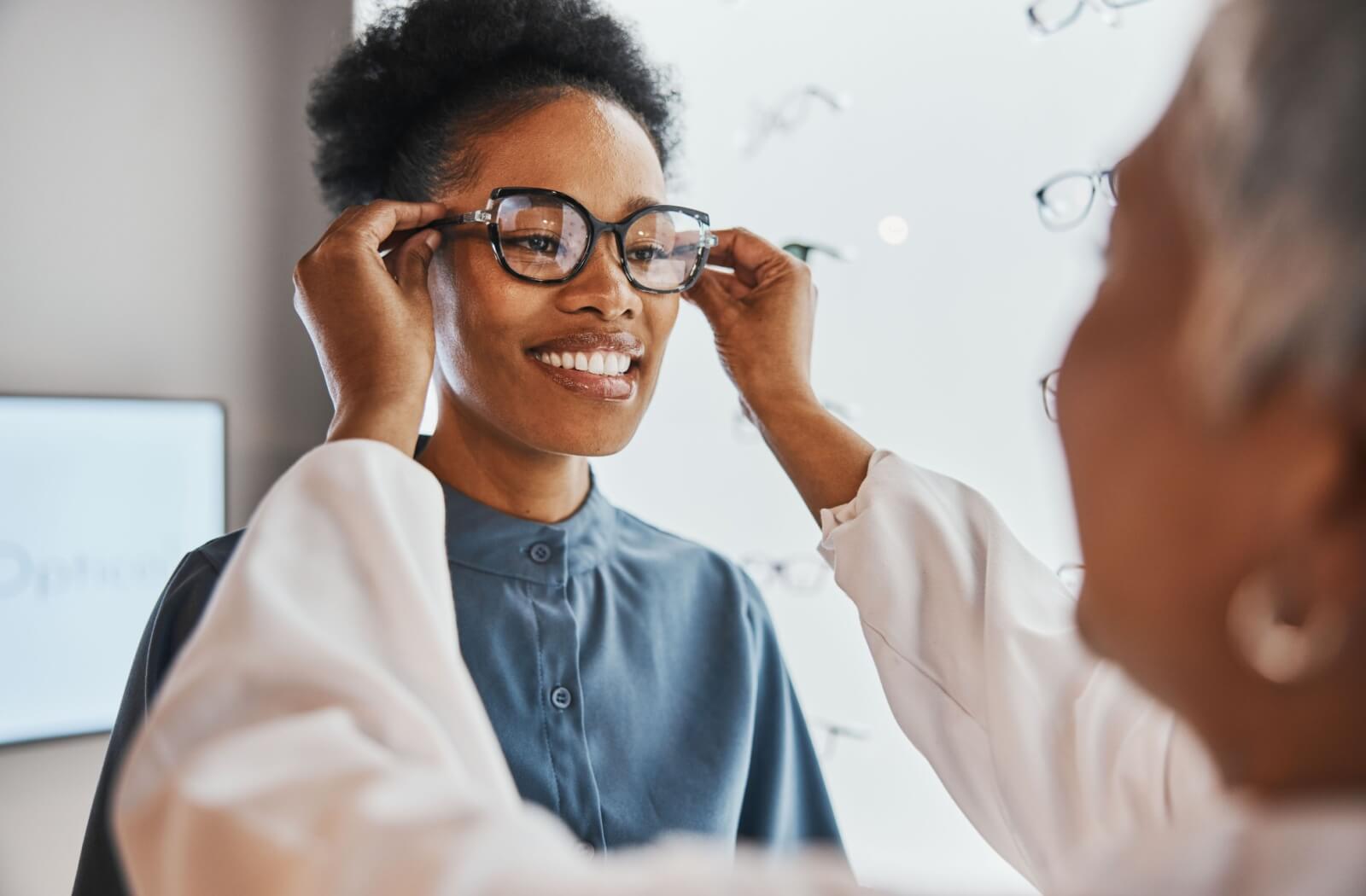 A person smiling and adjusting new black eyeglass frames during a fitting in an optical shop.