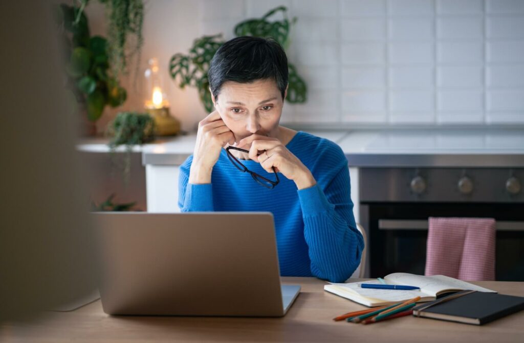 An individual looking at a laptop screen with a concerned expression while holding their eyeglasses.